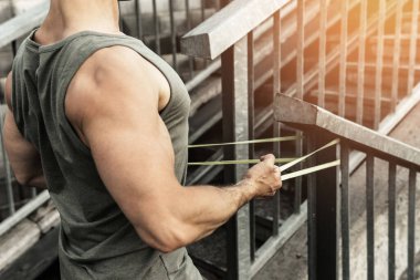 Genç ve kaslı bir adam antrenman sırasında sokakta lastik bantla direniyor.. 