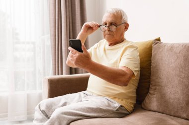 Gözlüklü adam evde akıllı telefon kullanıyor.