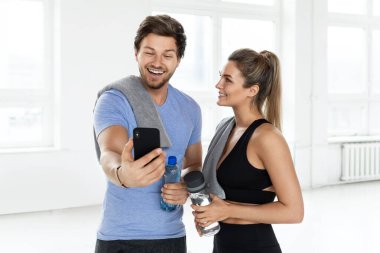 Spor salonundaki bir kadın ve erkek. Takım arkadaşına akıllı telefondan yeni bir fitness uygulaması gösteriyor..