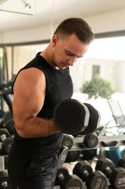 Sporcu adam spor salonunda çalışırken dambıllarla egzersiz yapıyor.