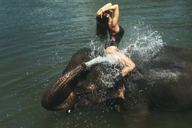 Mutlu genç kadın nehirde fille banyo yapıyor.