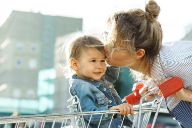 Genç, güzel anne ve küçük tatlı oğlu bir süpermarketin yanındaki alışveriş arabasında.