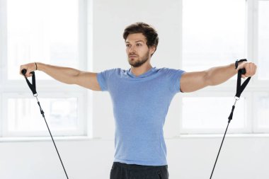 Spor salonunda lastik bantlarla antrenman yapan yakışıklı bir genç. Omuz yanal yükseltme egzersizi.