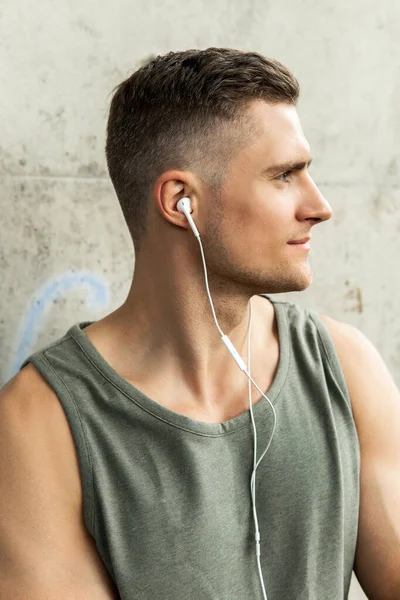 Portrait of a handsome man with an earphones. Listening music during a fitness workout on a street.
