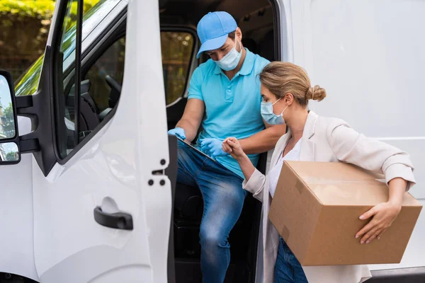 Prevention masks are new safety measures. Young woman receiving package from the delivery man on a van