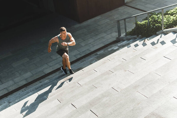 Muscular man is running upstairs by concrete staircase on the street