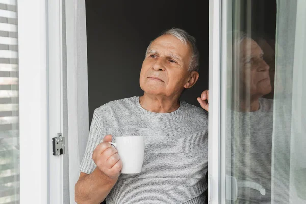 Elinde Bir Fincan Sıcak Kahveyle Pencereye Bakan Yaşlı Bir Adam — Stok fotoğraf