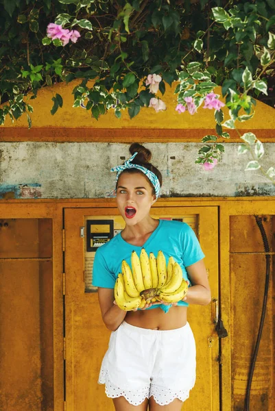 Young happy woman with a bunch of bananas posing beside old filling station
