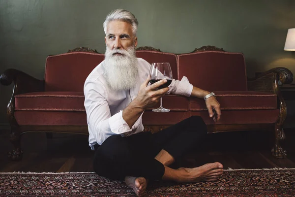 坐在地板上 喝着红酒的英俊而又时髦的大胡子老人 — 图库照片