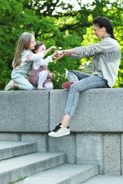 若い幸せな母親と彼女の2人の娘が座って街の公園で遊んでいます — ストック写真