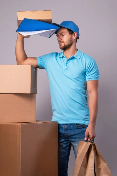 Tired delivery man during work with a packages in a cardboard boxes over gray background