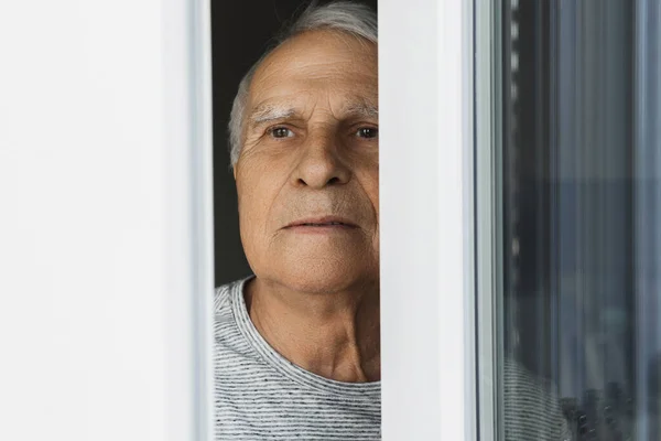 Portrait of lonely elderly man looking into the window