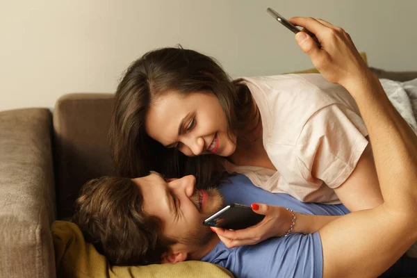Junges Lächelndes Paar Liegt Auf Dem Sofa Und Benutzt Smartphones — Stockfoto