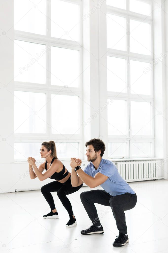 Fitness man and woman during workout with in the gym. Squats exercise for glutes and hips muscles.