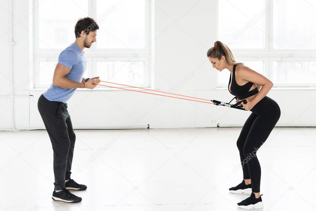 Young woman during workout with a personal fitness instructor using rubber resistance bands in the gym.