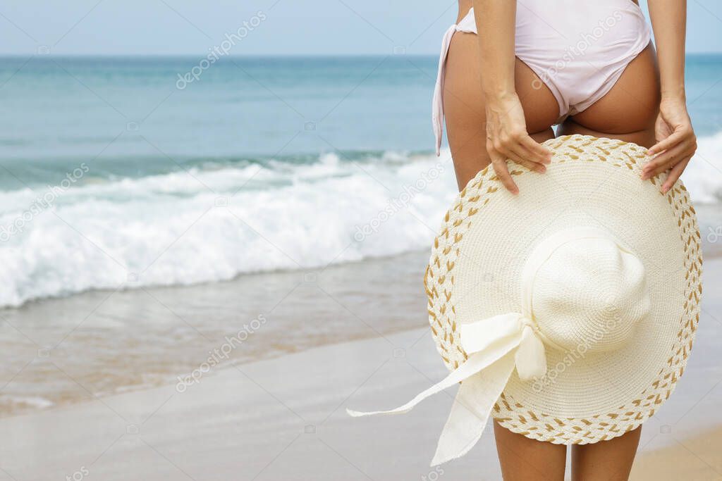 Summer vibes. Beautiful female body with a hat on the beach.