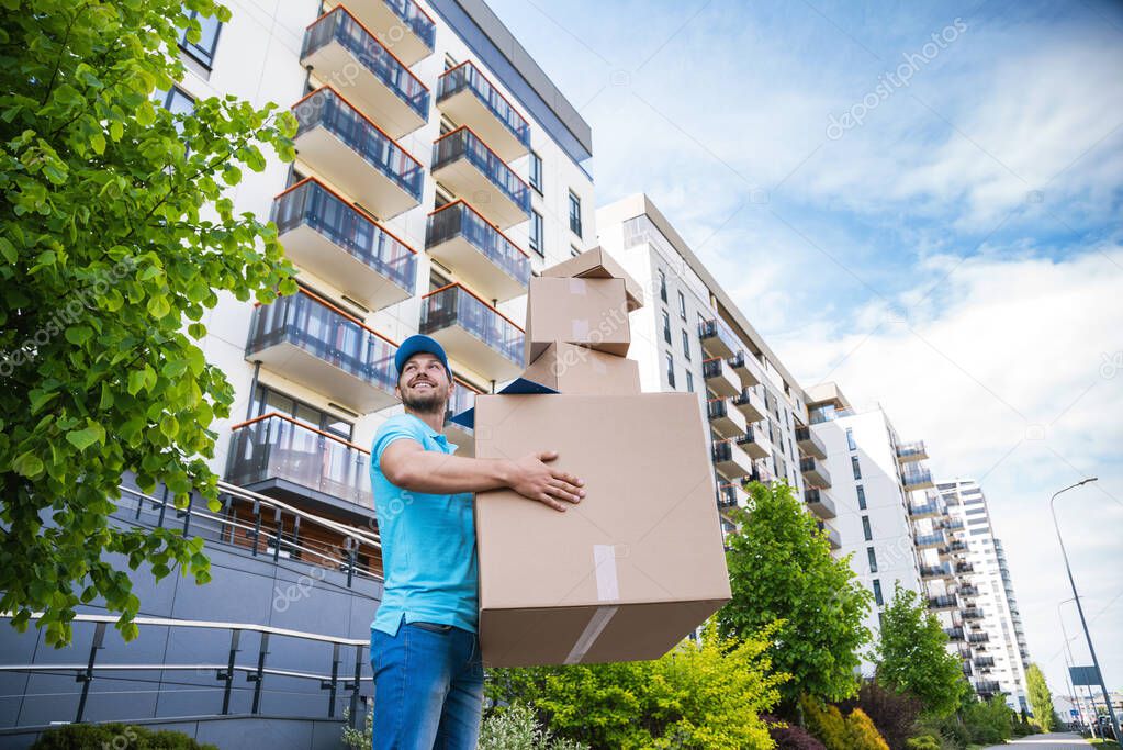 Strong delivery man holding a stack of a cardboard boxes on a city street