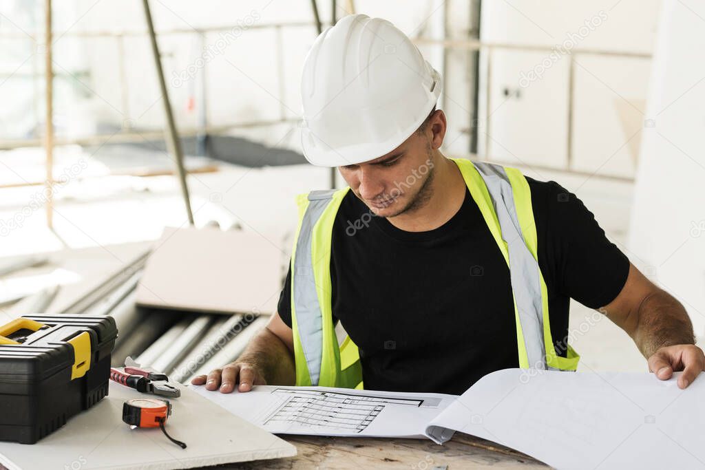 Young is worker checking blueprints during his work on a construction site