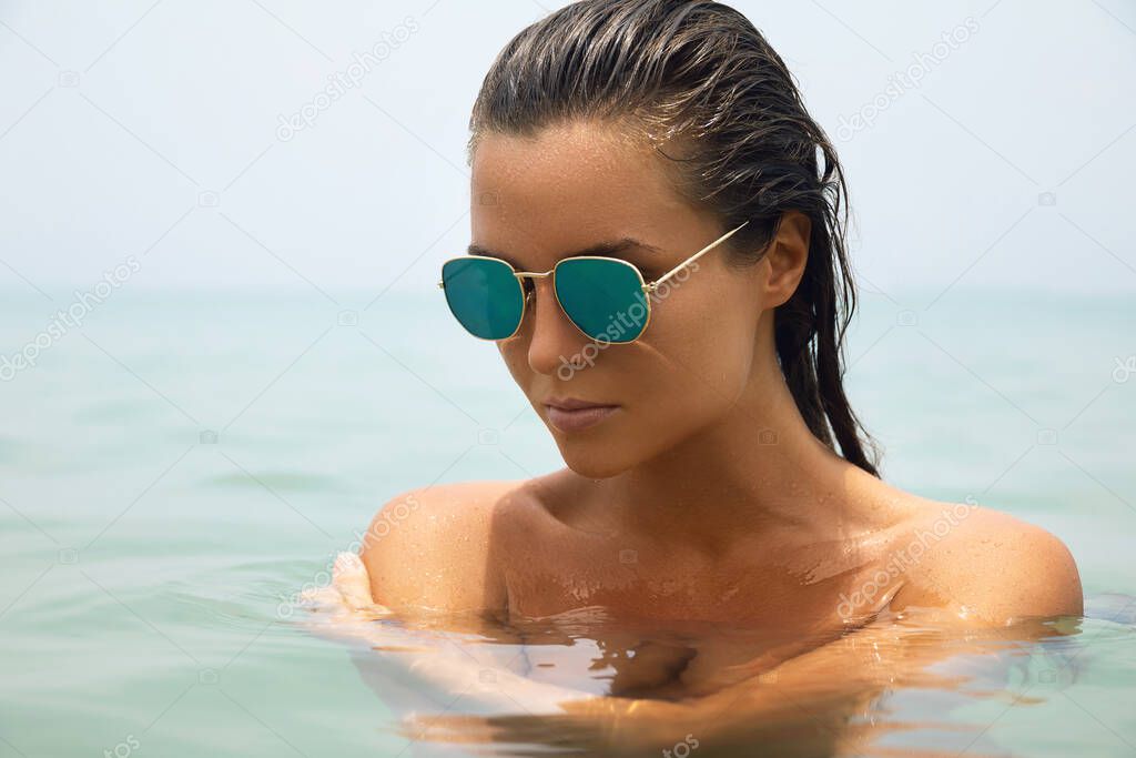 Beautiful wet woman is bathing in the sea wearing sunglasses 