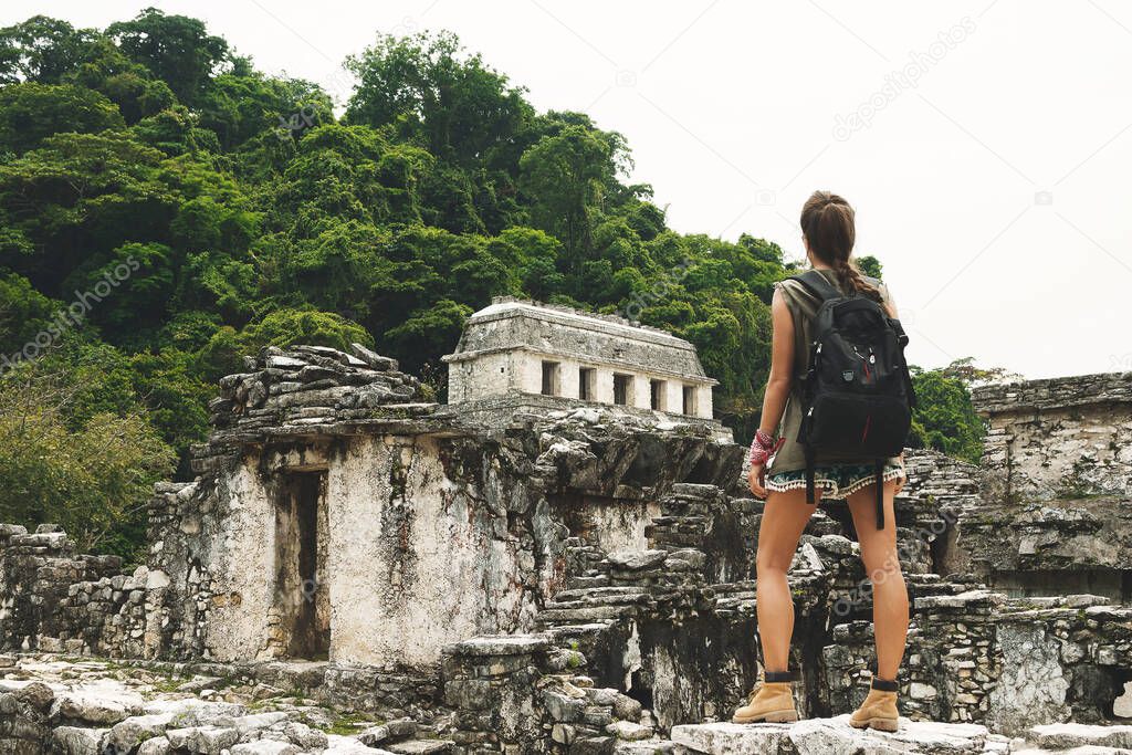 Hiker woman with a backpack looking at ancient Mayan ruins