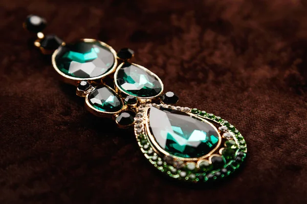 Luxury earrings with green gemstones on the brown velvet background