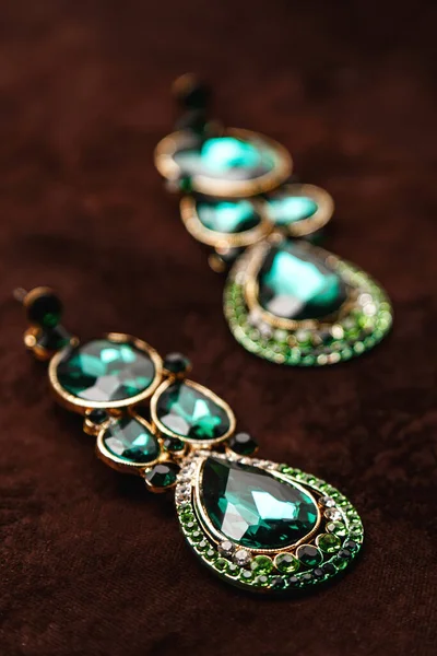 Luxury earrings with green gemstones on the brown velvet background