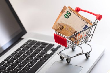 İçinde 50 Euro 'luk banknot olan minyatür alışveriş arabası. Online alışveriş ve e-ticaret kavramı.