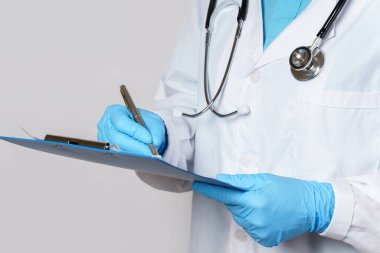 Doktor gri arka plan hakkında tıbbi rapor dolduruyor.