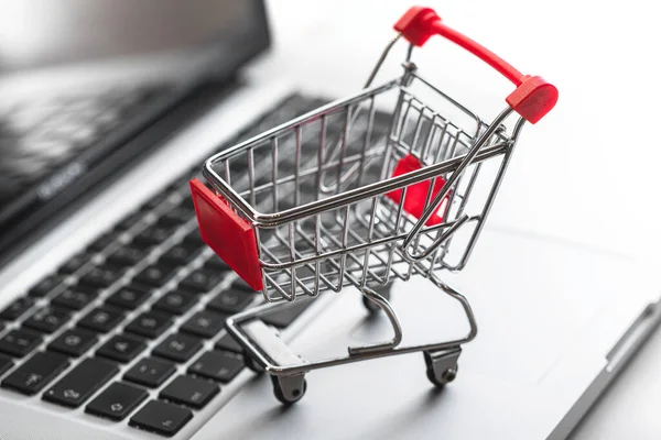 Dizüstü bilgisayarın klavyesinde minyatür alışveriş arabası. Online alışveriş ve e-ticaret kavramı.