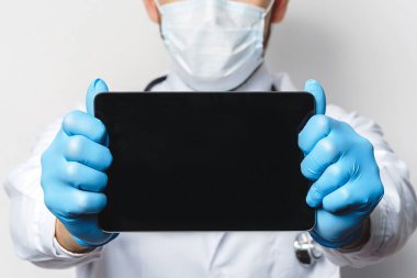Plastik eldiven giyen doktor elinde boş alanlı tablet bilgisayar tutuyor.