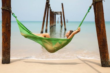 Genç kadın hamakta dinleniyor kırık iskeleden sarkan eski kirişlere asılı.