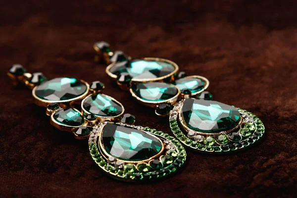 Luxury earrings with green gemstones on the brown velvet background