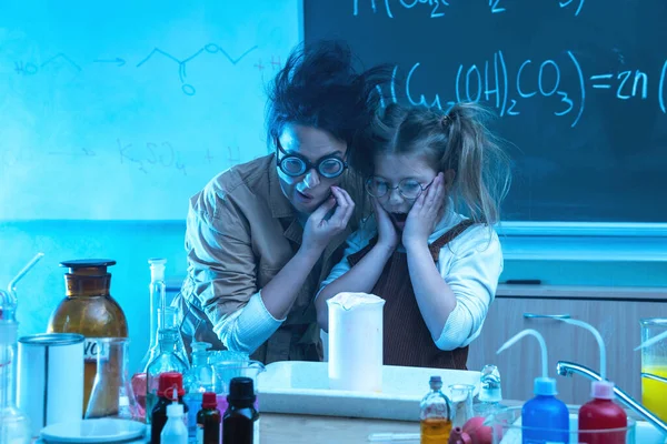 Funny teacher and little girl during chemistry lesson mixing chemicals in a laboratory