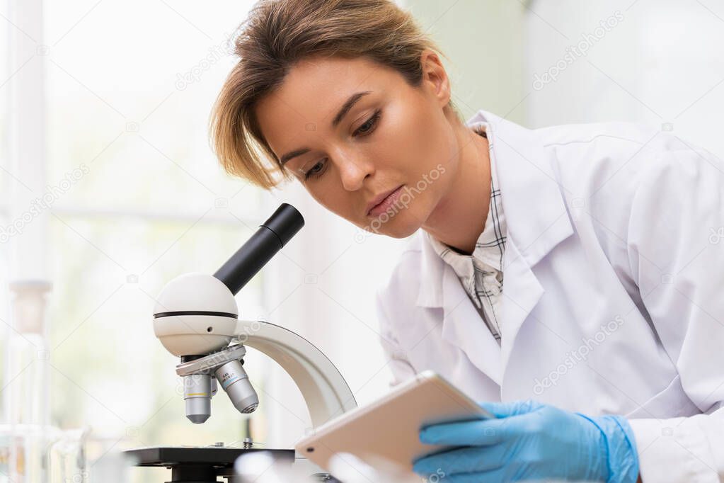 Woman scientist is using microscope and tablet pc in a laboratory during research work