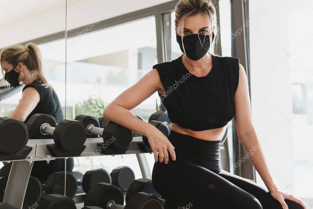 Gym new normal. Young athletic woman wearing a prevention face mask during her fitness workout.