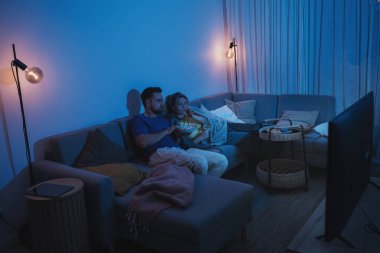 Kanepede bir kase patlamış mısır ve şarap paylaşan çift gece televizyon izliyor..