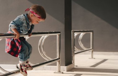 Kot elbise giyen ve açık hava ortamında metal korkuluklarda kırmızı bandana çalan tatlı çocuk..