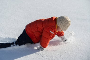 Güneşli bir günde parlak kış giysileri içindeki çocuk taze karda sürünüyor, neşeli açık hava aktivitesi ve kış eğlencesi konsepti.