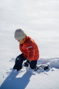 Karlı bir arazide, sakin bir kış gününde diz çöküp keşfe çıkan çocuk..