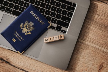 ABD pasaportu ve tahta bloklar dizüstü bilgisayarda yazım işi, çalışma vizesi konsepti, uzak iş veya dijital göçebe seyahat izni.