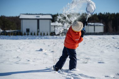 Banliyöde güneşli bir kış gününde kürekle kar atan bir çocuk..