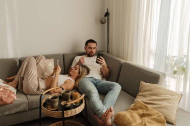 Çift, yakınlarda atıştırmalık eşliğinde akıllı telefonlar kullanarak koltukta dinleniyor..