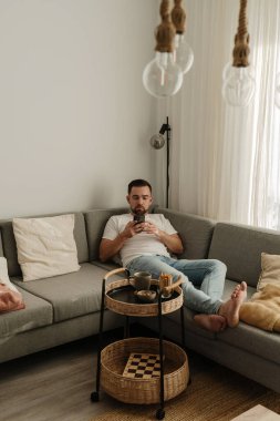 Adam akıllı telefon ve atıştırmalıklarla evdeki koltukta dinleniyor..