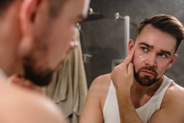 Banyodaki aynanın önünde göz bandı altında başvuran bir adam..