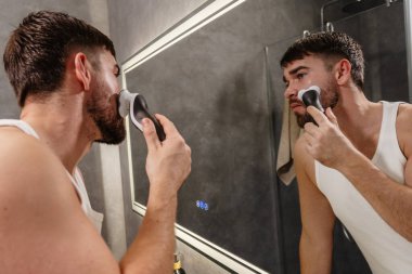 Adam aynaya bakarken yüzünü jiletle traş ediyor..