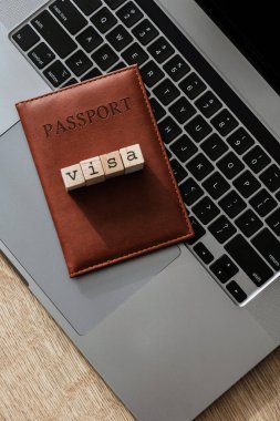 Laptop klavyesinde vize harfi blokları olan kahverengi pasaport sahibi, uluslararası seyahat sembolü.
