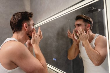 Banyodaki aynanın önünde göz bandı altında başvuran bir adam..