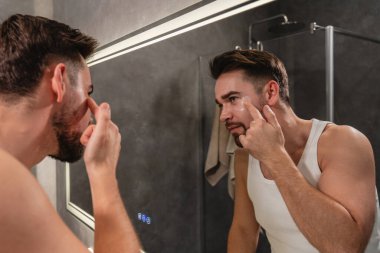 Banyodaki aynanın önünde göz bandı altında başvuran bir adam..