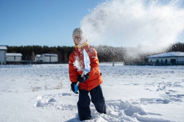 Banliyöde güneşli bir kış gününde kürekle kar atan bir çocuk..