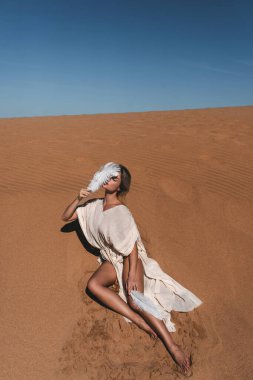 Keten bornozlu kadın Kum Kumulunda Beyaz Tüylü Dinleniyor.